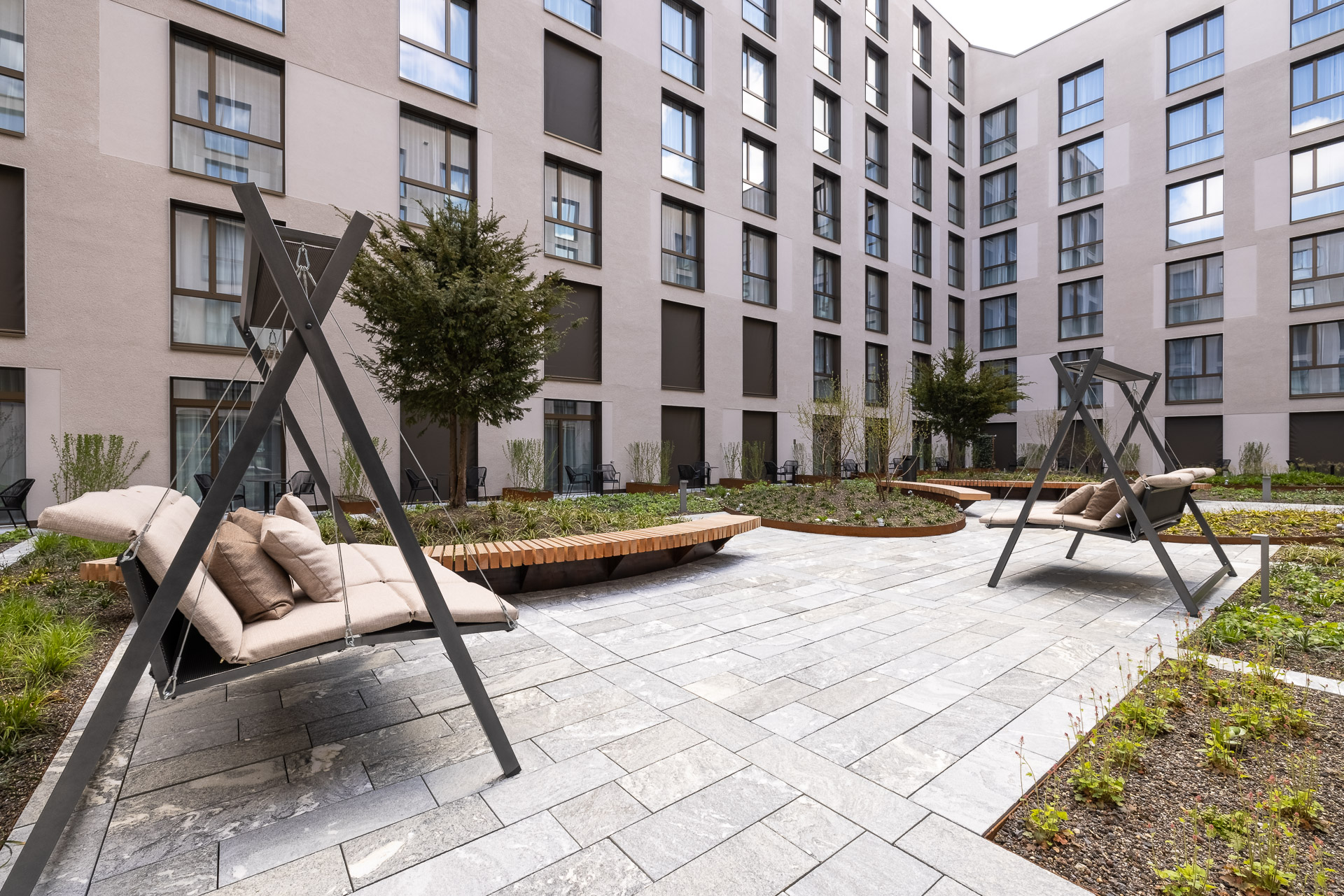 The beautifully landscaped courtyard with some plants and comfortable swings at JOYN Zurich.